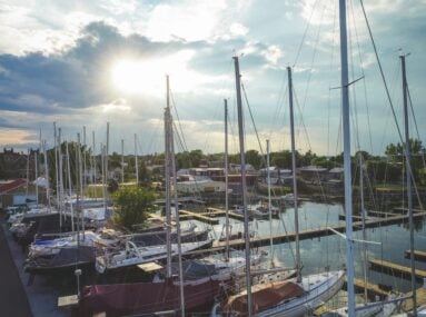 lots of sailboats docked at marina and sun shining through clouds