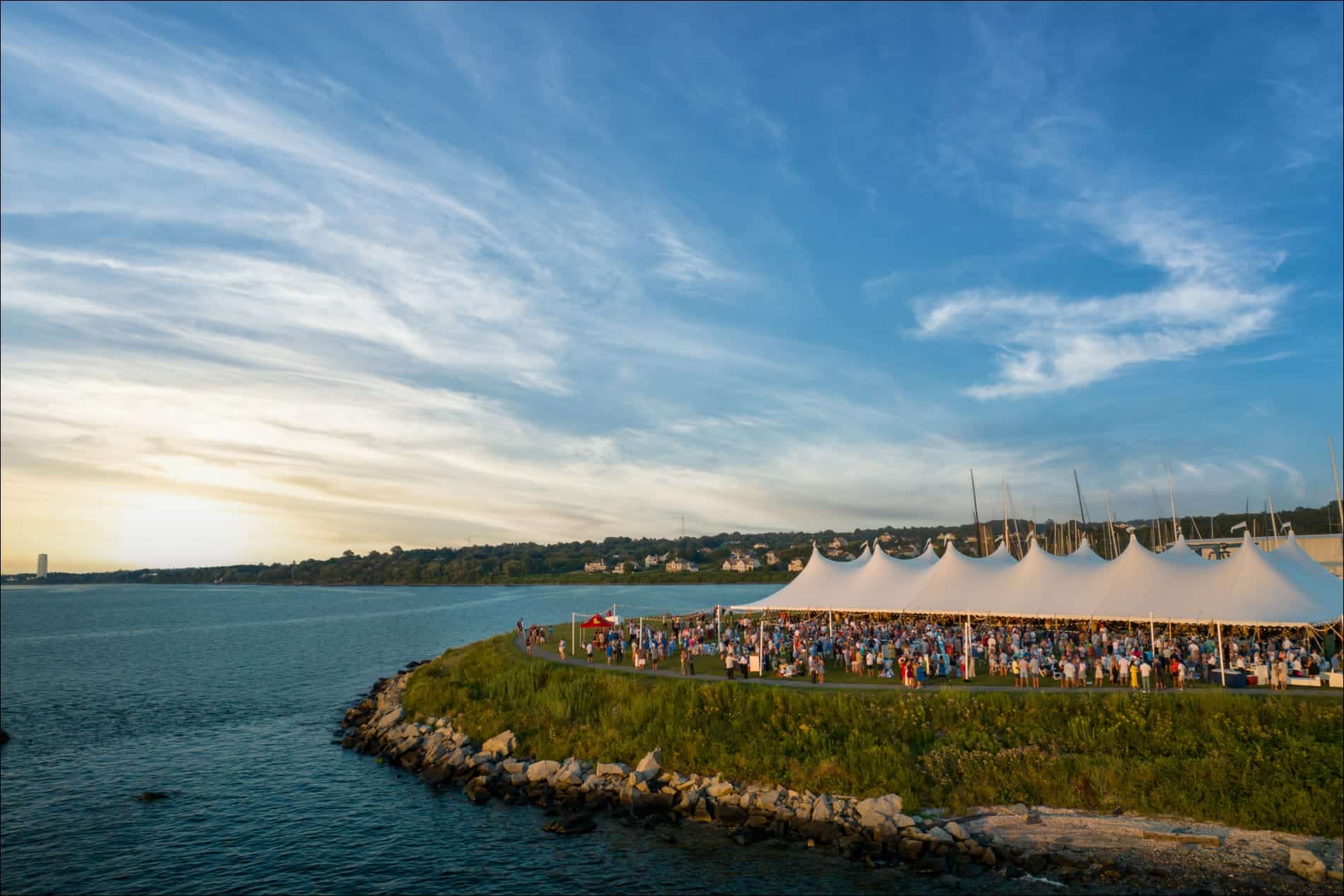 una gran multitud bajo una carpa junto al agua al atardecer